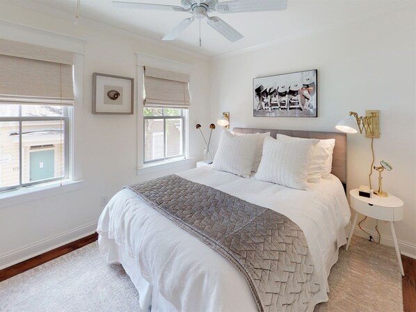 A bedroom with a bed, a ceiling fan, a window with blinds, a bedside table with a lamp, and a wall-mounted artwork. - Heated Pool Access | 5*Clean | Flex Cancelation (Savannah)