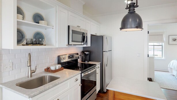 A modern kitchen with white cabinetry, stainless steel appliances, a marble countertop, and a pendant light.