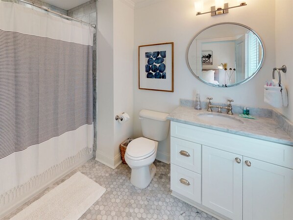 Une salle de bain avec des toilettes blanches, un lavabo en marbre, un miroir et une œuvre d’art encadrée accrochée au mur.