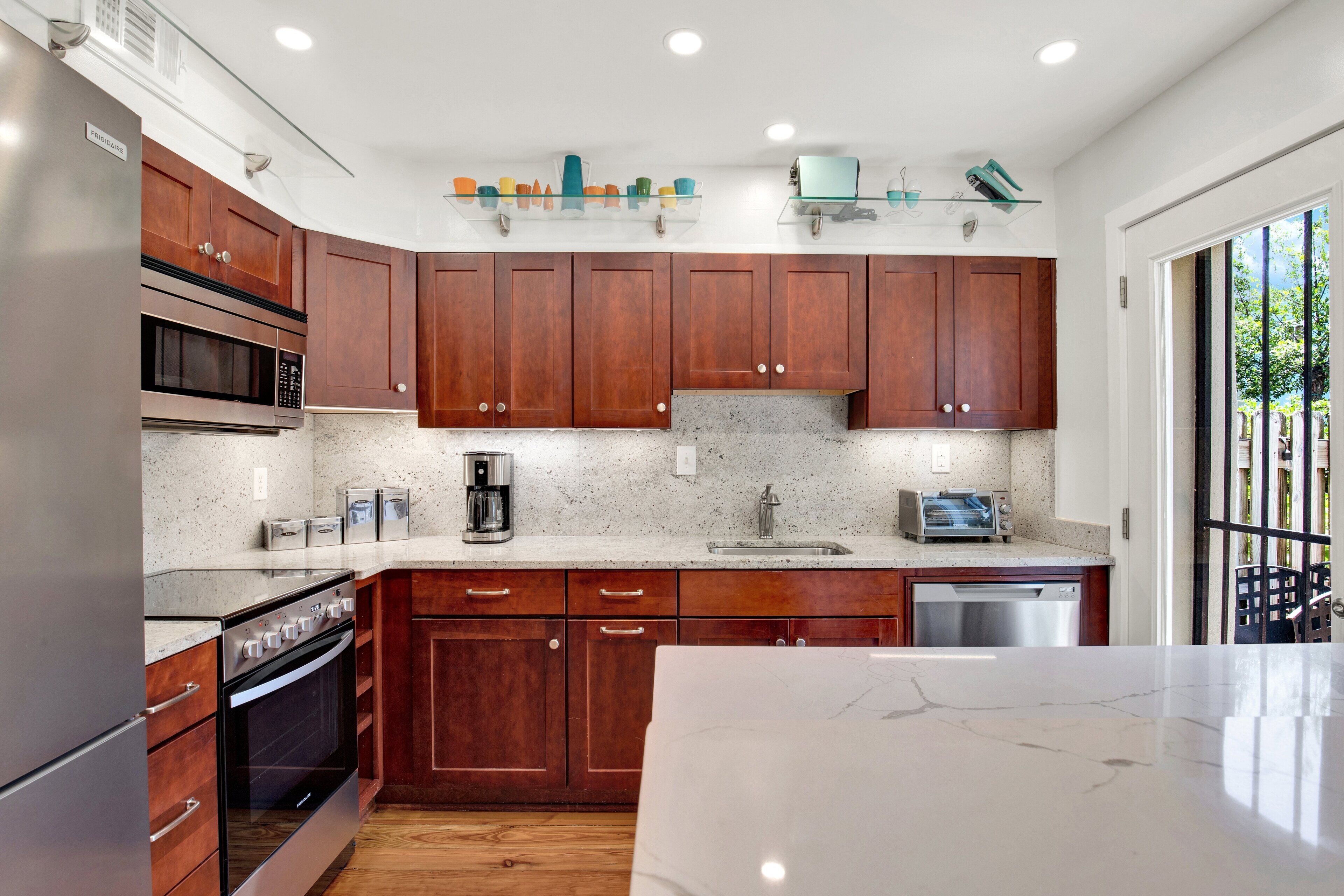 A modern kitchen with wooden cabinets, stainless steel appliances, and a marble countertop.