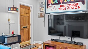 A living room with a large flat-screen TV, a vintage radio, and a wooden cabinet. - Heated Pool Access | 5*Clean | Flex Cancelation (Savannah)