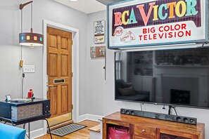 A living room with a large flat-screen TV, a vintage radio, and a wooden cabinet. - Heated Pool Access | 5*Clean | Flex Cancelation (Savannah)