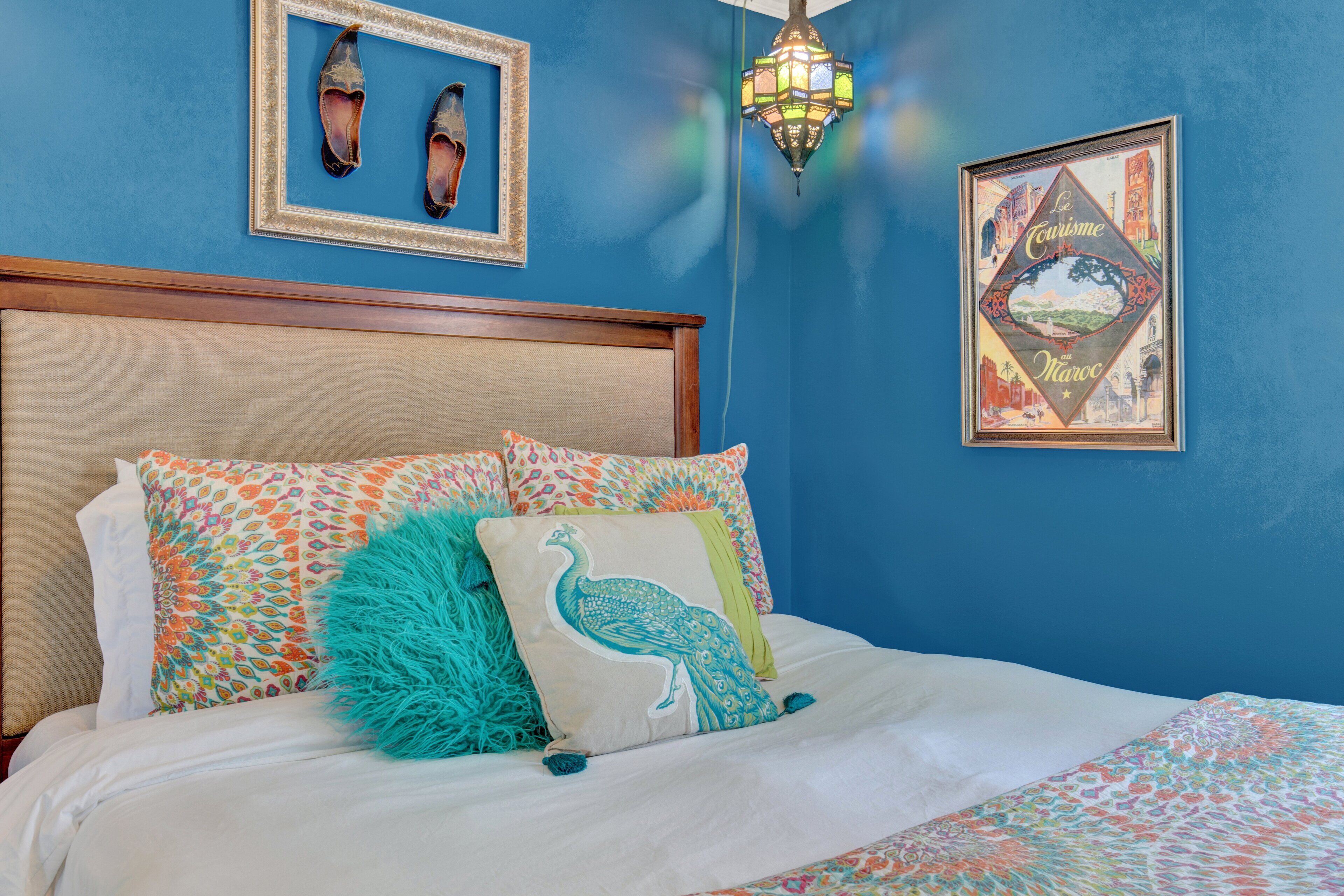 A bedroom with a blue wall, a wooden headboard, and a bed with white bedding and colorful pillows.