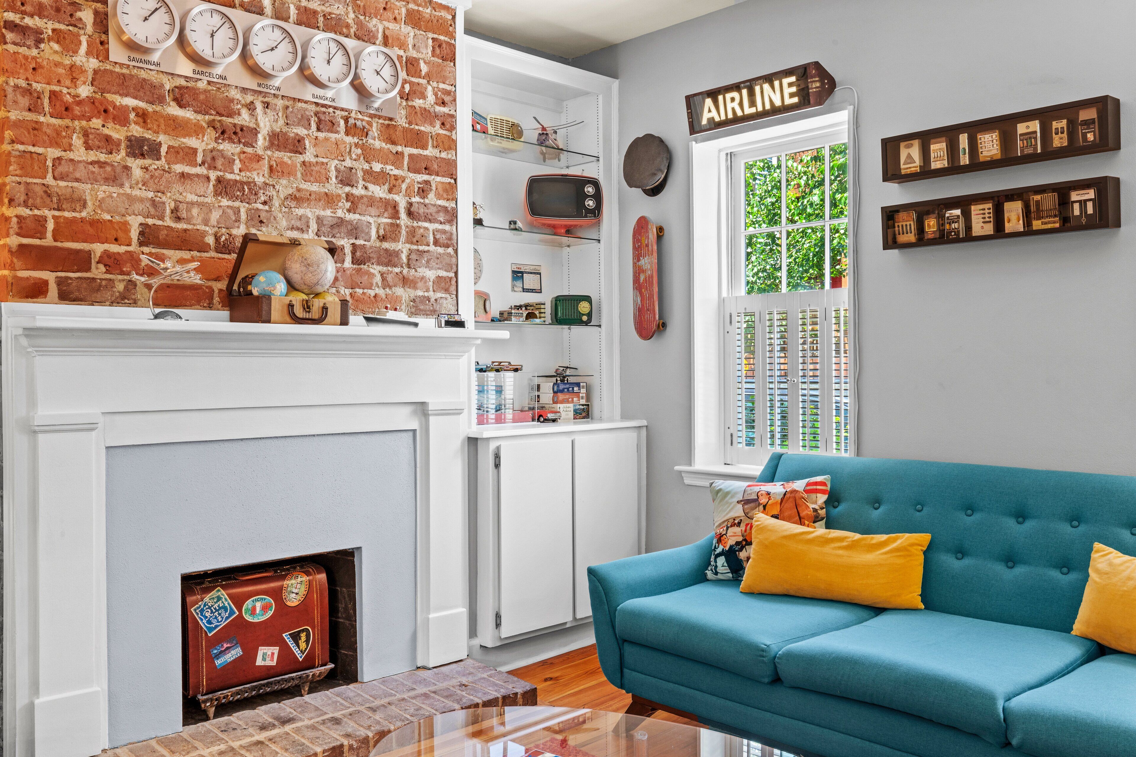 A living room with a brick wall, a fireplace, a blue sofa, and a window with blinds.