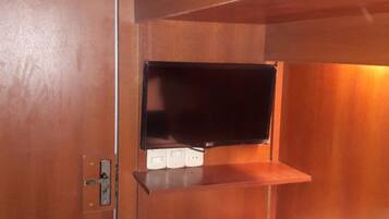 Una cama litera con una cama baja y un estante arriba, en una habitación con paredes de madera y un enchufe a la vista.
