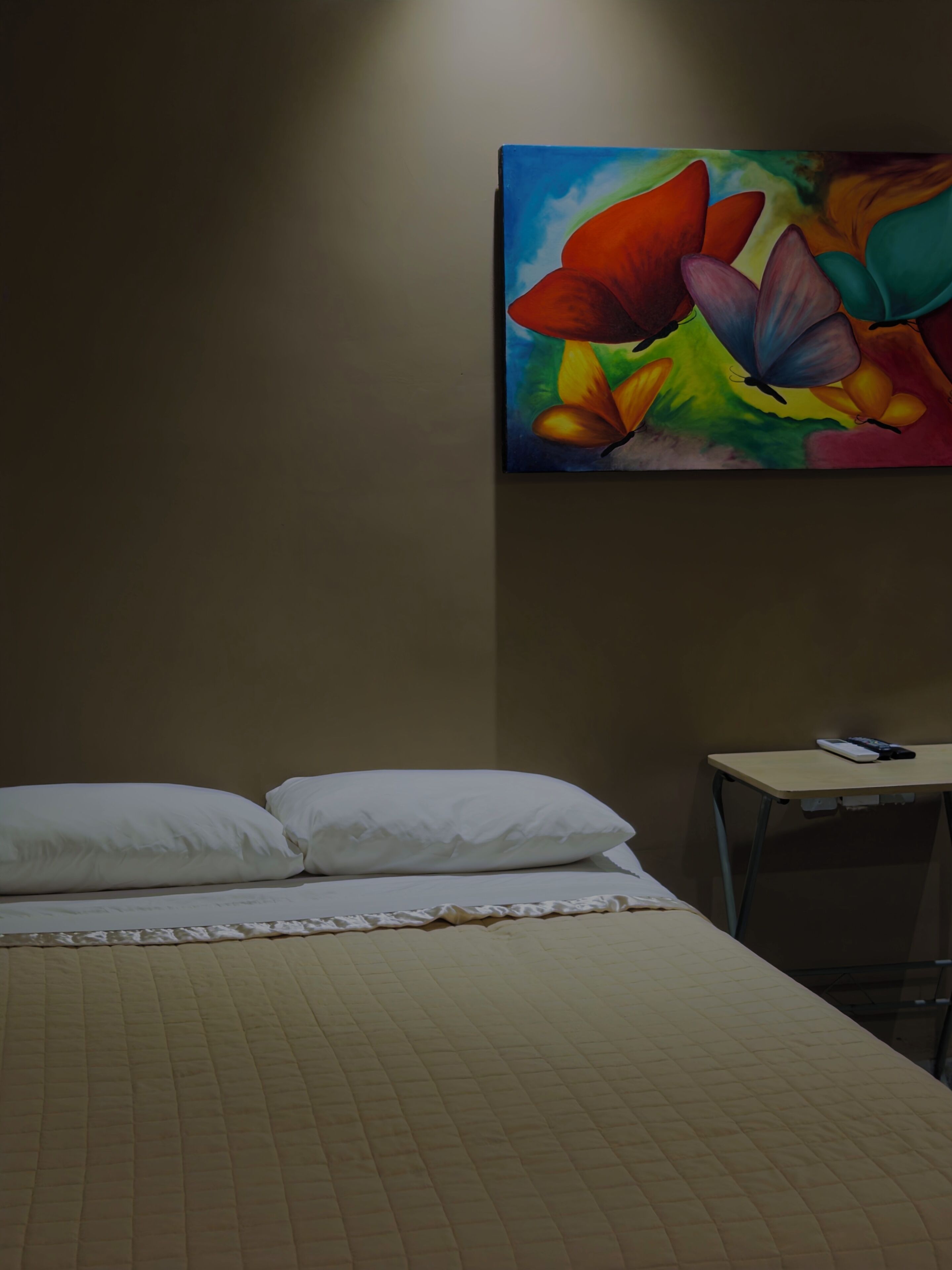 A hotel room with a bed, pillows, a desk, and a colorful painting on the wall.