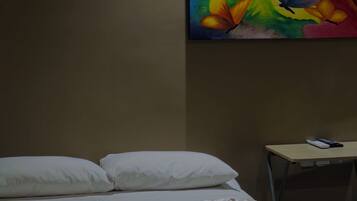 A hotel room with a bed, pillows, a desk, and a colorful painting on the wall.