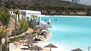 Un complexe hôtelier de bord de mer doté de chaises longues et de parasols, d’une piscine et d’un bâtiment avec une terrasse offrant une vue sur l’eau.
