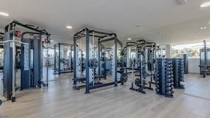 Une salle de sport équipée de divers appareils de musculation, de miroirs et dotée d’un plancher en bois.