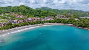 A coastal town with a curved bay, dense greenery, and buildings along the shoreline. - Oceanfront•Sleeps 6•Full Kitchen•BBQ•Pool•Balcony - Alouatta Guesthouse (Las Catalinas)