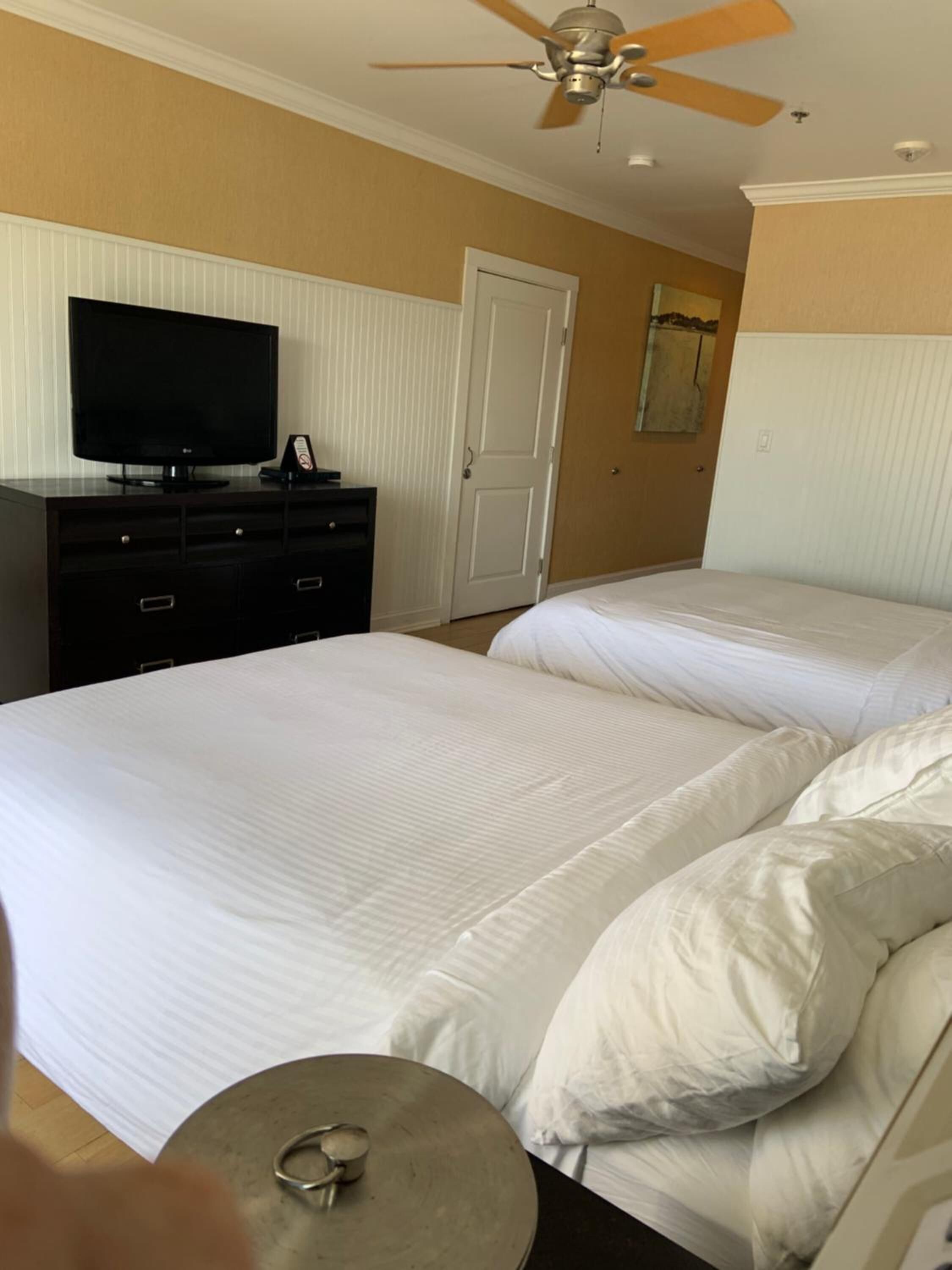 Una habitación de hotel con dos camas, un televisor en un tocador, un ventilador de techo y una puerta.