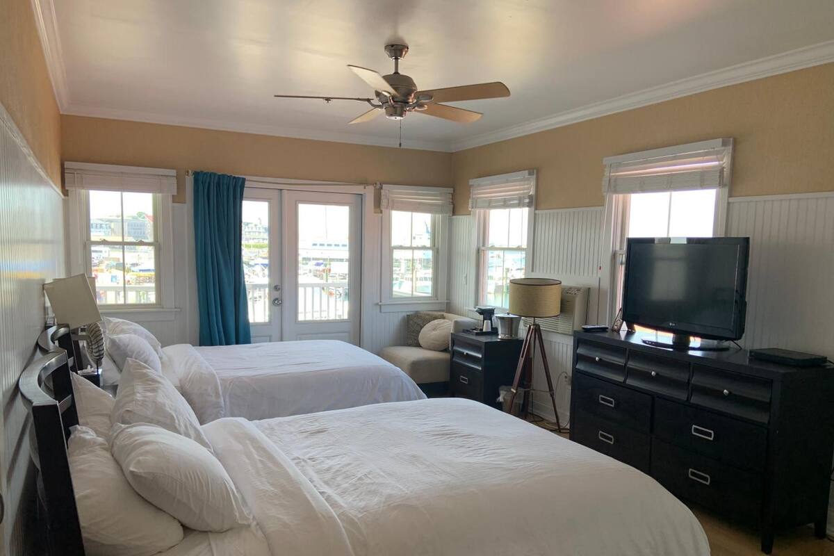 A hotel room with two beds, a ceiling fan, a TV, and a desk with drawers.