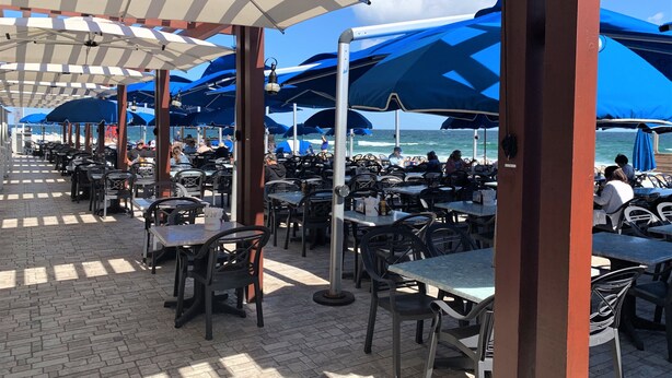 An outdoor dining area with tables and chairs under umbrellas, overlooking the ocean. - Ballard's (Block Island)