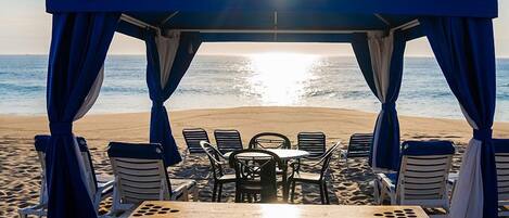 A beach tent with a table and chairs, overlooking the ocean.