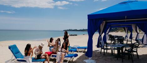 A beach with lounge chairs and a blue tent.