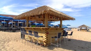 A beachside bar with a thatched roof, surrounded by blue umbrellas and beach chairs. - Ballard's (Block Island)