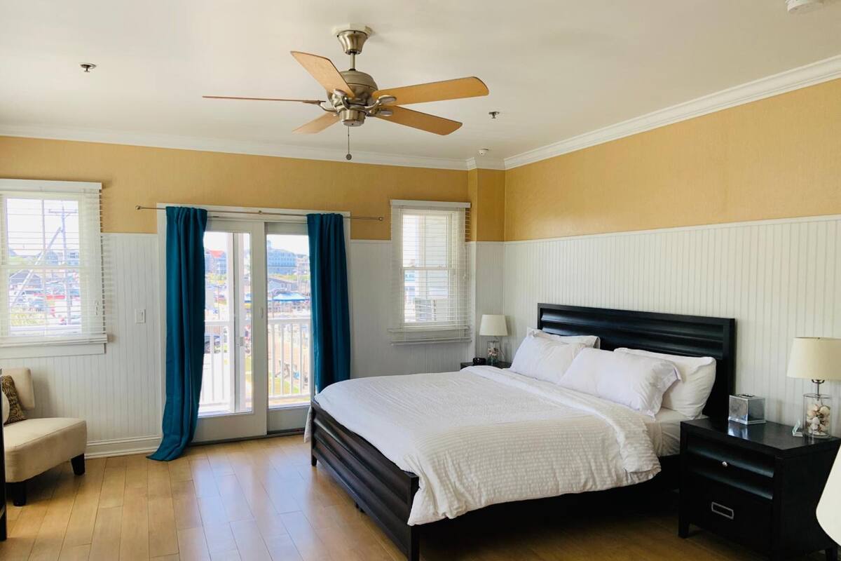 A bedroom with a bed, a nightstand, a chair, a ceiling fan, and a view through the door.