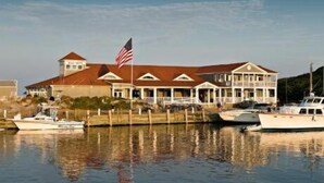 A large waterfront property with multiple buildings, including a prominent house with a red roof and an American flag. There are boats docked in the water in front of the property. - Ballard's (Block Island)