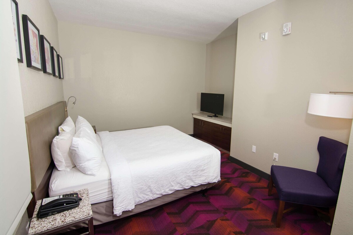 A hotel room with a bed, a chair, a television, and a desk.