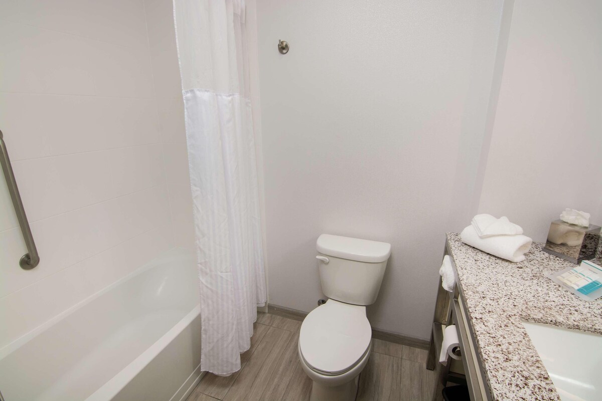 A bathroom with a toilet, a shower curtain, a sink with a towel, and a toilet paper holder.