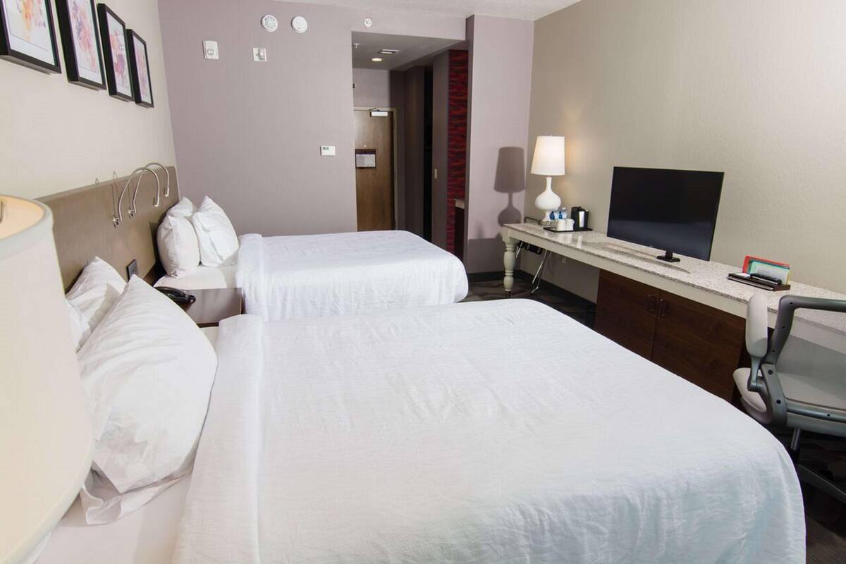 A hotel room with two beds, a desk with a computer, a chair, and a TV.
