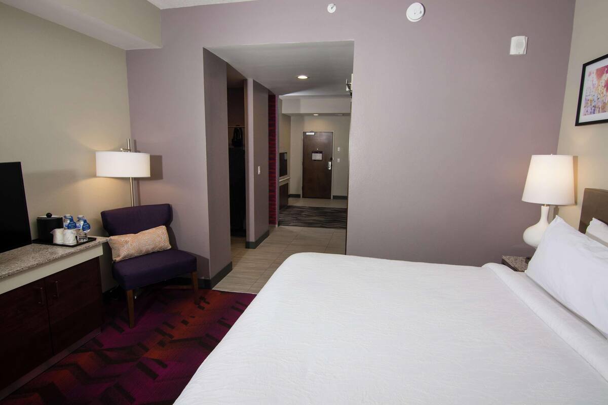 A hotel room with a bed, a desk, a chair, two lamps, and a carpeted floor.