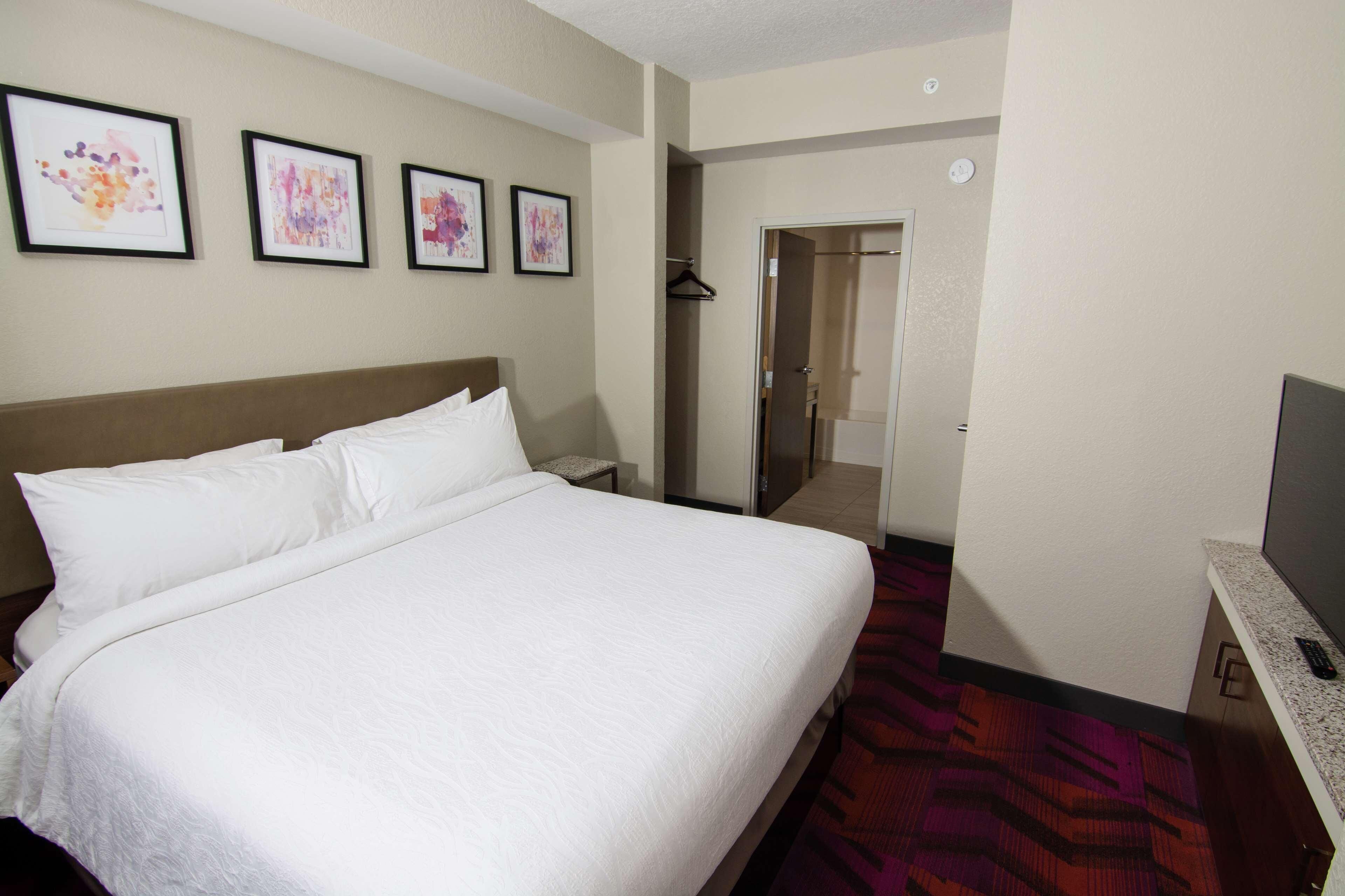 A hotel room with a large bed, a TV, a wardrobe, and framed artwork on the wall.