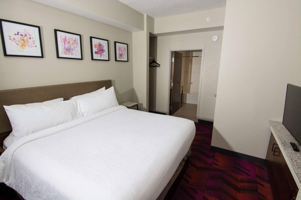 A hotel room with a large bed, a TV, a wardrobe, and framed artwork on the wall.