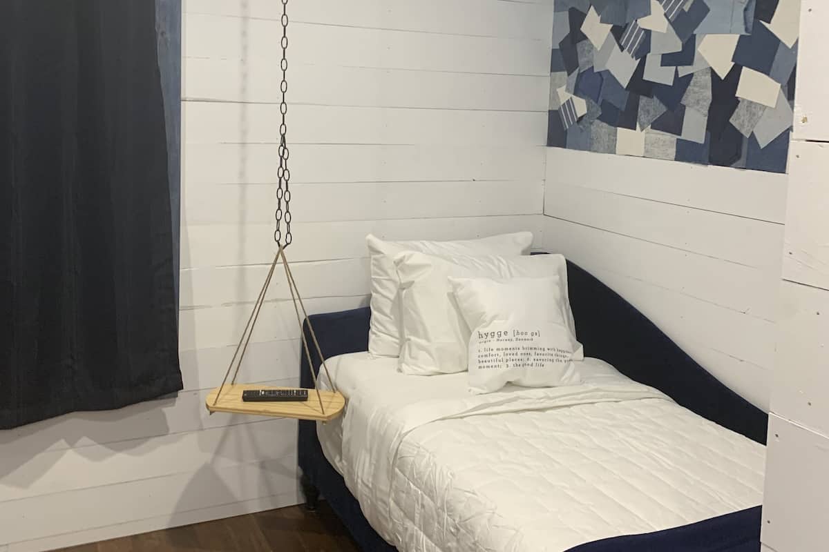 A bedroom with a bed, a hanging swing, a patterned ceiling, and a wooden floor.
