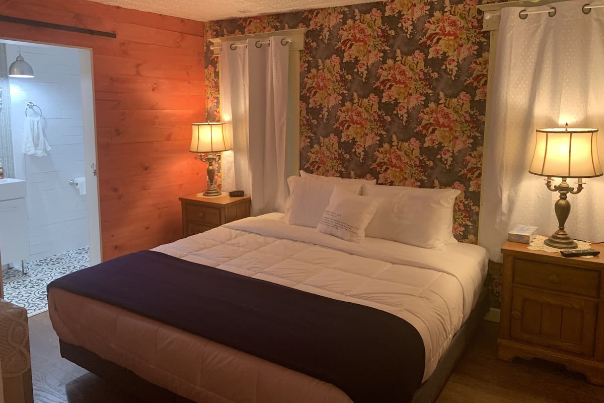 A bedroom with a wooden headboard, floral wallpaper, two bedside lamps, a bed with white bedding, and a wooden nightstand.