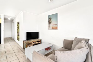 A living room with a flat-screen TV on a white coffee table, a beige sofa, and a painting of a beach scene.