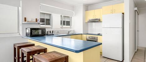 Una cocina moderna con una isla central, taburetes de bar, microondas, estufa y refrigerador.