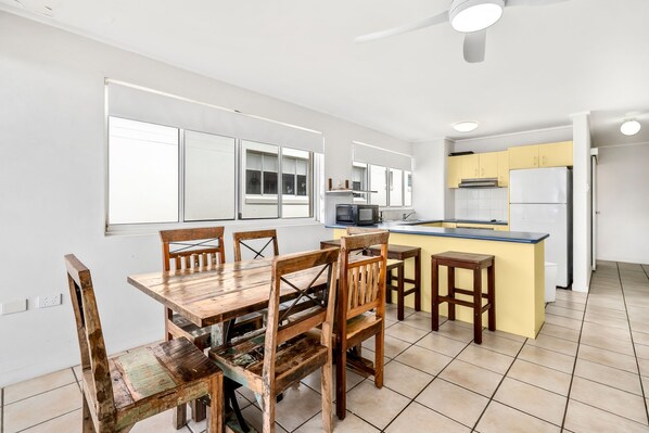 A kitchen with a dining area, white walls, and a ceiling fan.