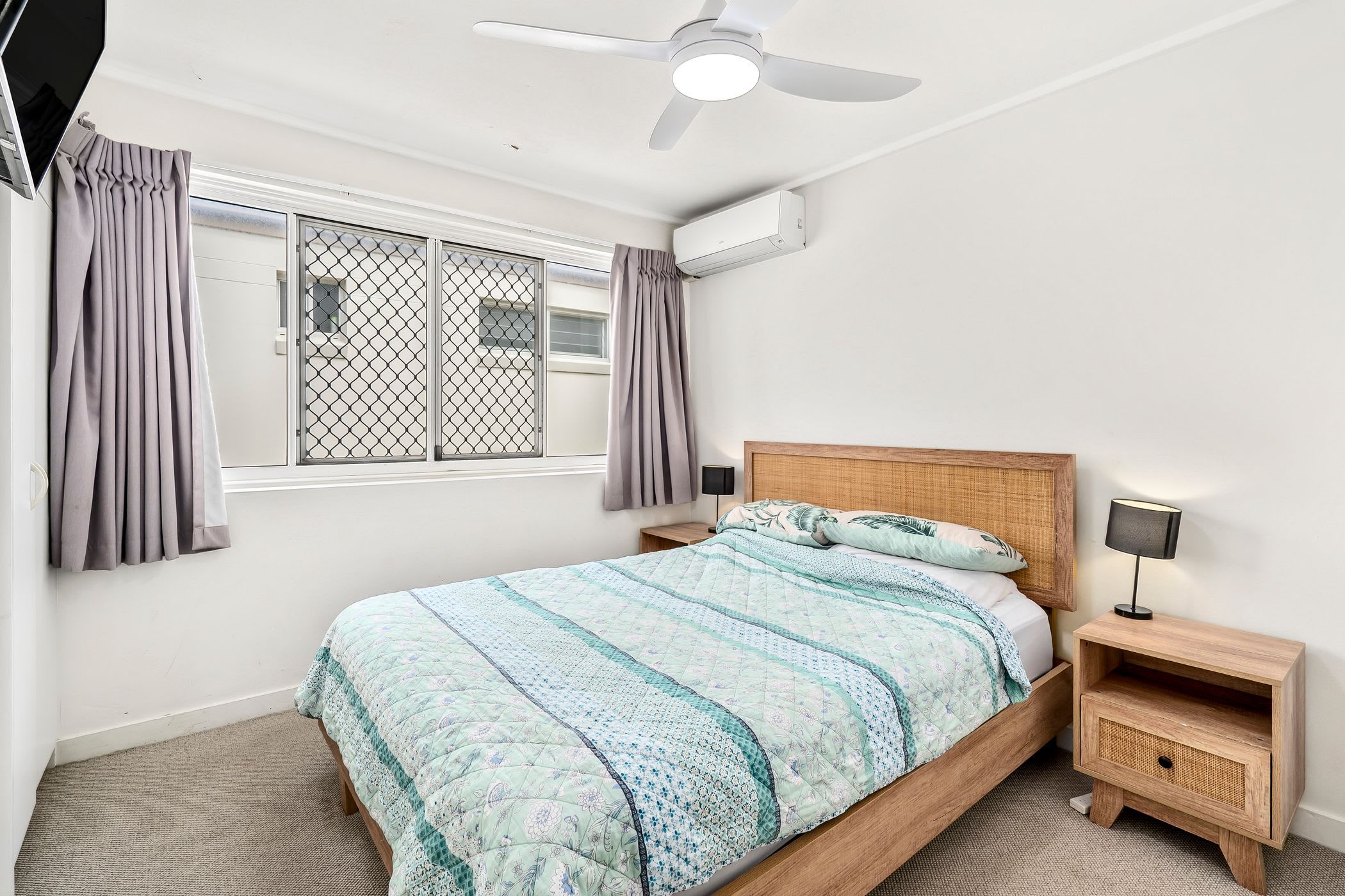 Ein Schlafzimmer mit einem Bett, einem Nachttisch, einer Lampe, einem Deckenventilator und einem Fenster mit Vorhängen.