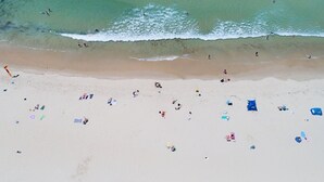 An aerial view of a beach with people, umbrellas, and beach chairs.