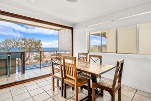 Un coin repas avec une table et des chaises en bois, une vue sur la mer et un balcon doté d’une balustrade.