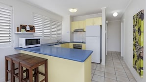 A kitchen with a blue countertop, white cabinets, a white refrigerator, a microwave, and wooden stools.
