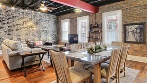 A cozy living room with a brick wall, a sofa, a coffee table, and a dining area with a table and chairs. - Heated Pool Access | 5*Clean | Flex Cancelation (Savannah)