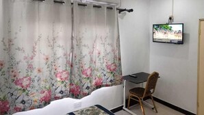 Una habitación con una cama, un escritorio, una silla, un televisor y una ventana con cortinas florales.