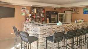 Una zona de bar con mostrador de piedra, taburetes negros y un refrigerador lleno de bebidas.