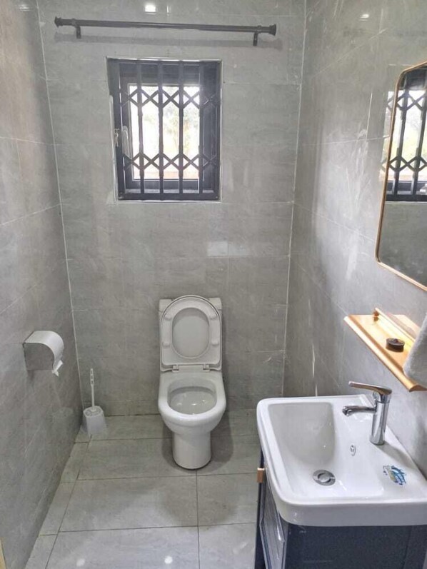 A small, modern bathroom with a toilet, sink, and a window with bars.