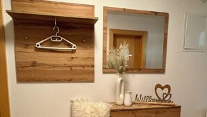 A bathroom with a wooden vanity, a hanging clothes rack, a mirror, and a fluffy white pillow.
