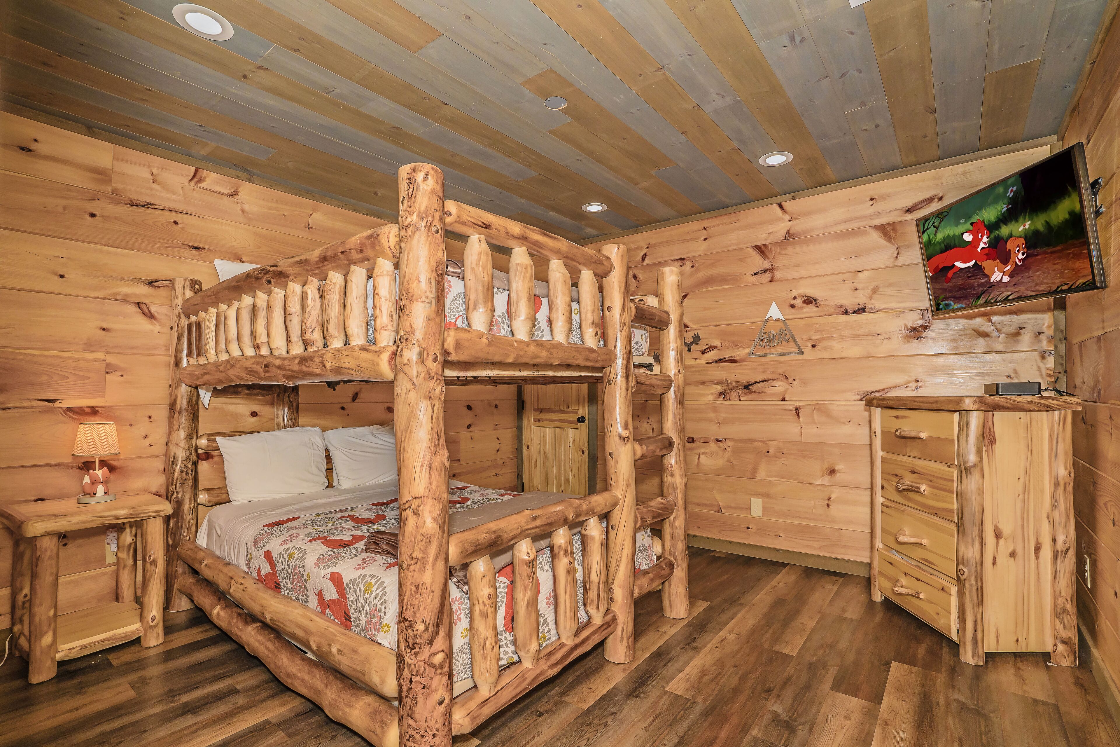 A wooden cabin room with a bunk bed, a small desk, and a television on the wall.
