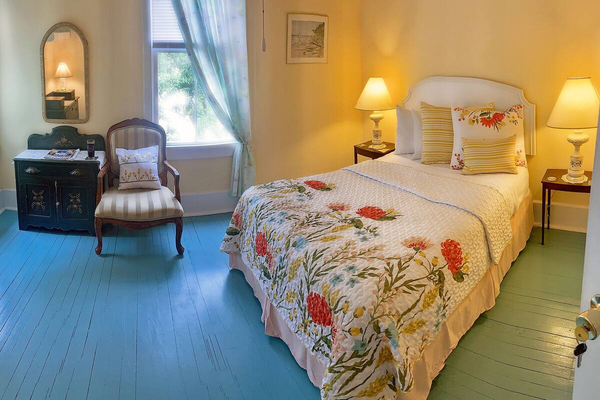 A bedroom with a bed, a chair, a dresser, and a window with curtains.