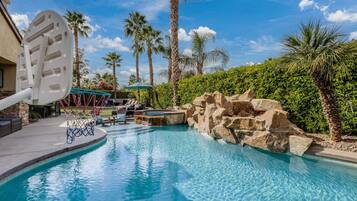 Relax by the serene pool surrounded by palm trees and a natural stone wall.