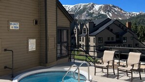A pool area with a sign indicating a spa capacity of 8 persons, surrounded by buildings and a mountain backdrop. - Walk to Ski LIft, 2 Master Suites WIFI & Garage (Mammoth Lakes)