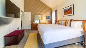 A hotel room with a large bed, a wooden headboard, a flat-screen TV mounted on the wall, a mirror, a bedside table with a lamp, and a red bench. - Walk to Ski LIft, 2 Master Suites WIFI & Garage (Mammoth Lakes)