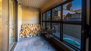 A covered outdoor area with a wooden table and chairs, a stack of firewood, and a view of neighboring houses through large windows. - Walk to Ski LIft, 2 Master Suites WIFI & Garage (Mammoth Lakes)