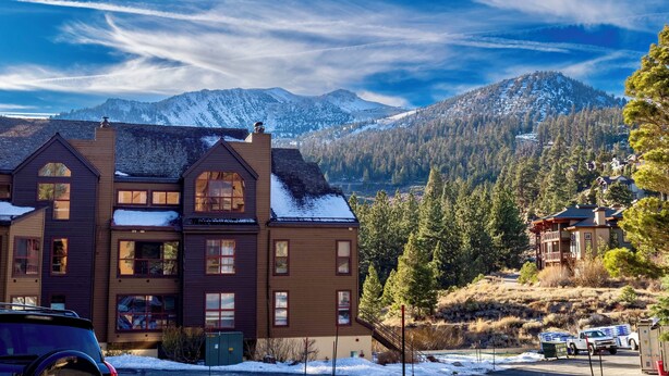 A multi-story building with large windows and a snow-covered roof, set against a backdrop of mountains and a clear sky. - Walk to Ski LIft, 2 Master Suites WIFI & Garage (Mammoth Lakes)