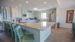 A spacious kitchen with a large island, light blue cabinets, and a wooden floor. - Experience oceanfront luxury at Ohana Tides, a 5-bedroom retreat in Holden Beach. (Holden Beach)